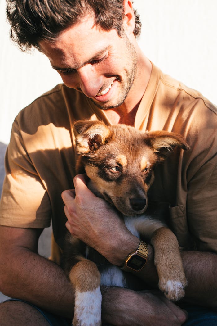 about-04 Smiling man embraces a cute puppy outside on a sunny day, expressing joy and companionship.